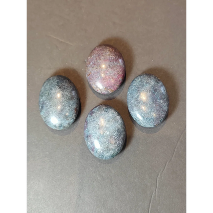 Four polished oval-shaped ruby kyanite spheres featuring deep gray and pinkish hues with speckled patterns