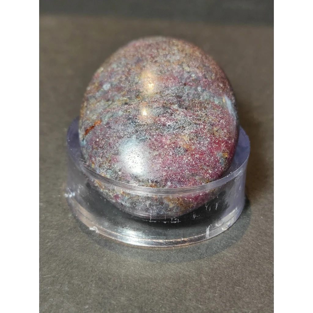 A polished ruby kyanite palmstone with mottled deep red purple and metallic silver hues displayed on a clear stand