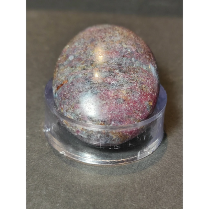 A polished ruby kyanite palmstone with mottled deep red purple and metallic silver hues displayed on a clear stand