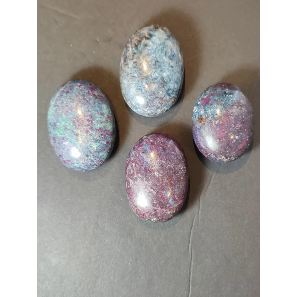 Four polished oval ruby kyanite polished spheres with speckled deep purple blue and green hues displayed on white background