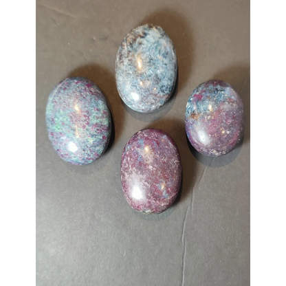 Four polished oval ruby kyanite polished spheres with speckled deep purple blue and green hues displayed on white background