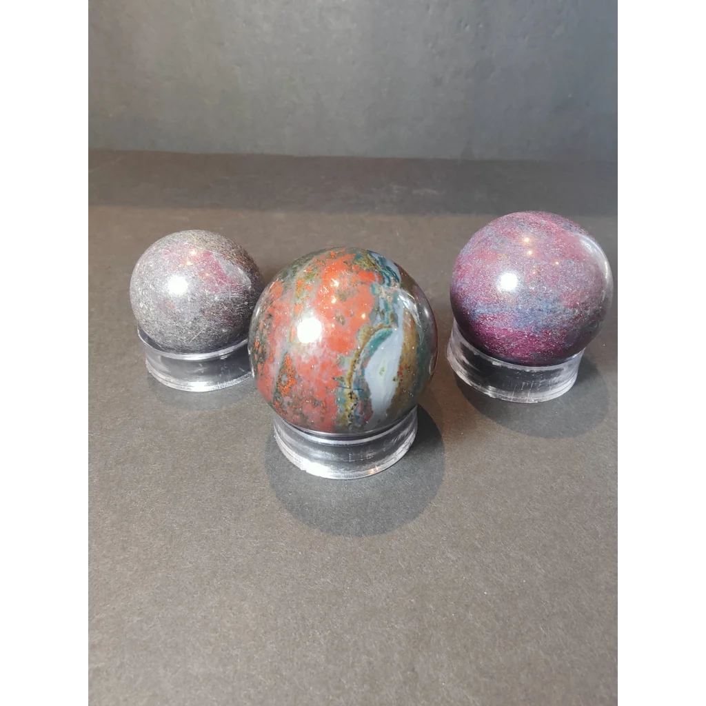 Three ruby kyanite polished spheres with swirling red orange purple and gray patterns on clear acrylic stands