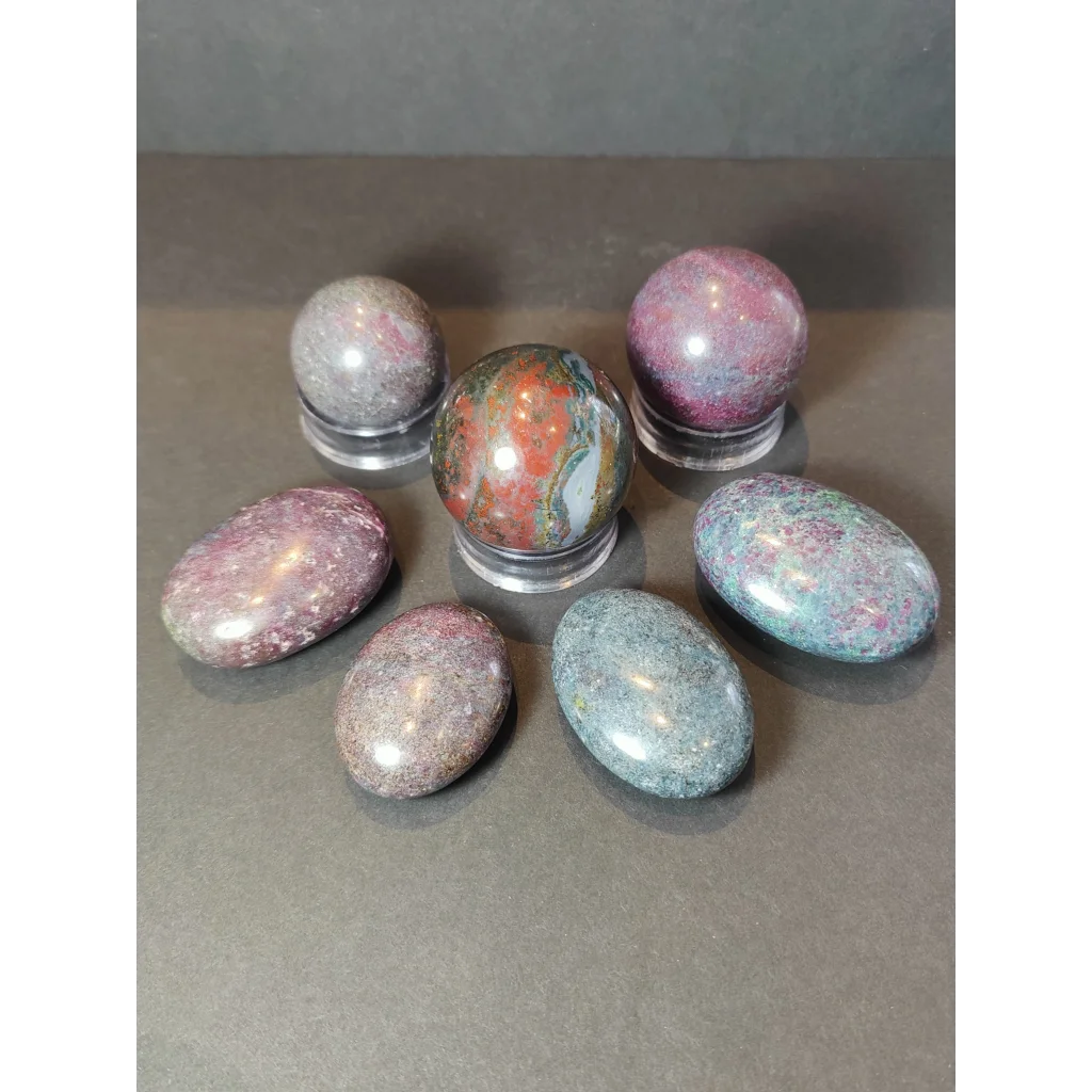 A collection of multicolored polished jasper stones alongside ruby kyanite polished spheres and palmstones