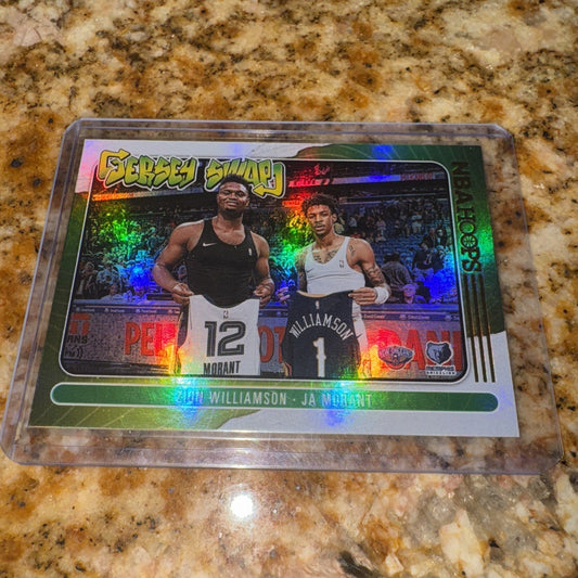 Holographic basketball card featuring Zion Williamson and Ja Morant in jerseys, displayed flat on speckled granite countertop with rainbow light refraction visible.