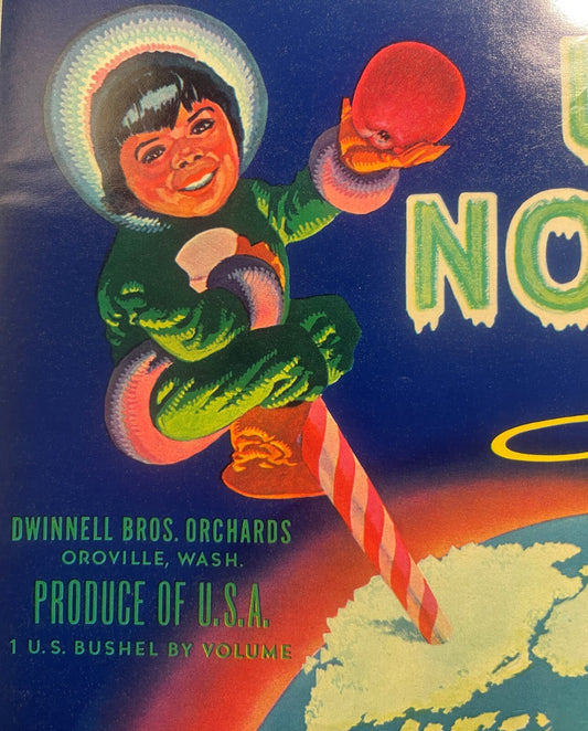 Close-up of the Up North apples label: the Inuit child in a fur-trimmed parka with a red apple on the striped pole, and the lines DWINNELL BROS. ORCHARDS, OROVILLE, WASH., PRODUCE OF U.S.A., 1 U.S. BUSHEL BY VOLUME