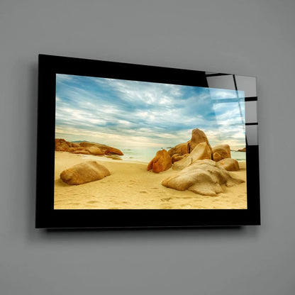 Black-framed glass wall art of golden rocks on sandy beach under blue sky