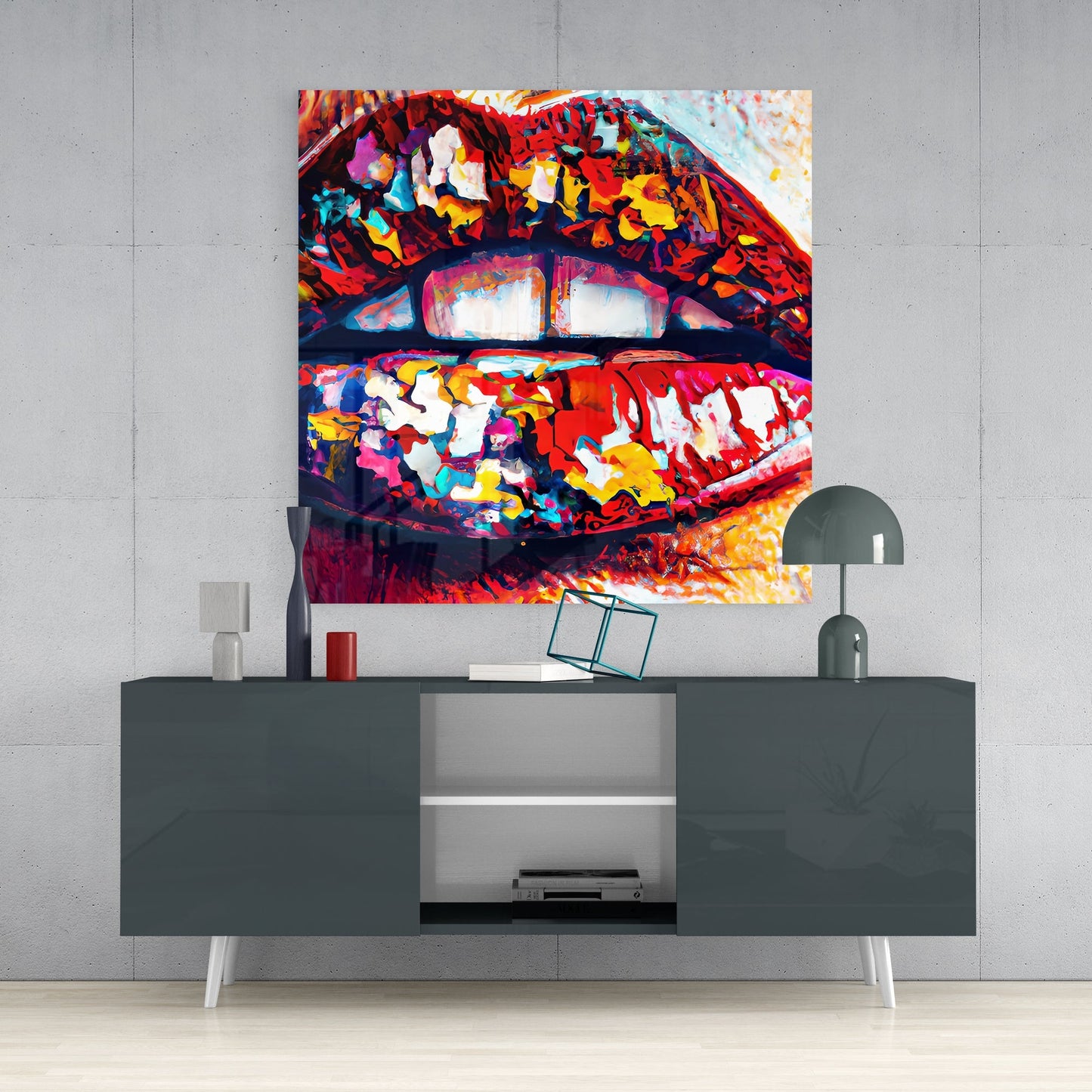 Vibrant multicolored pop art lips glass wall art hung above a dark gray media console in a modern interior setting.