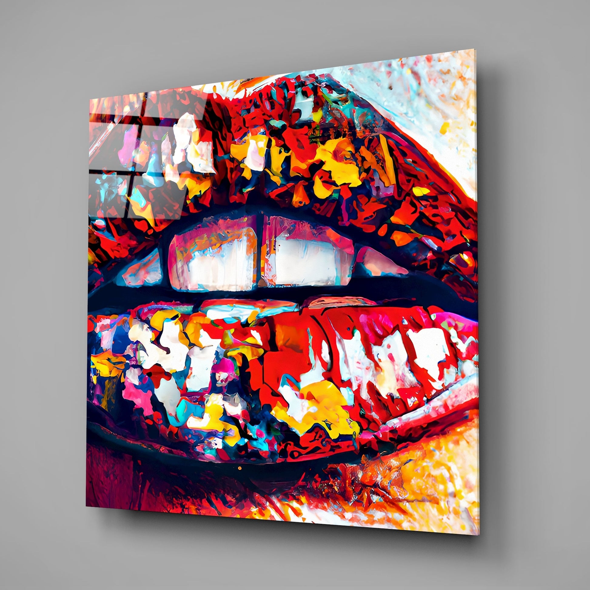 Angled view of vibrant multicolored glass wall art featuring abstract lips design with red, yellow, blue, and white sections mounted on gray wall.
