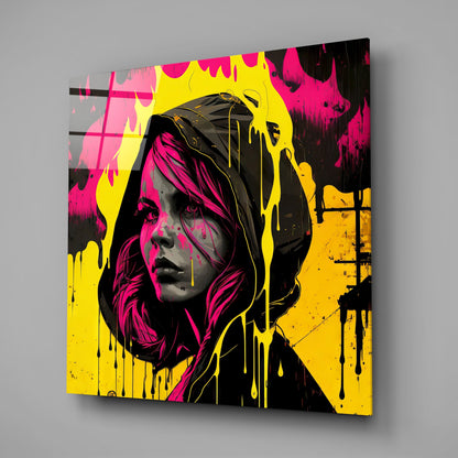 Glass wall art panel displaying a woman's face in magenta and black with yellow and orange paint drips, angled three-quarter view.