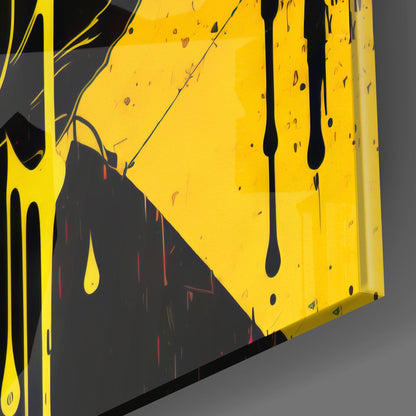 Close-up angled view of yellow glass wall art with black drips and red streaks on dark background, showing glossy surface and dimensional edges.