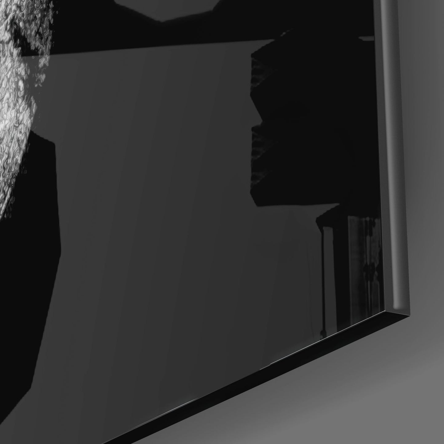 Low-angle side view of black glass wall art panel mounted on light gray wall in dim lighting.