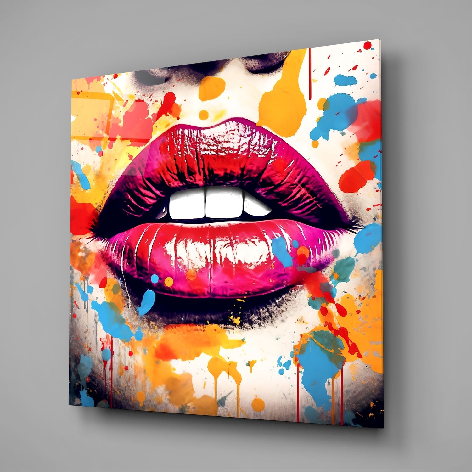 Angled view of glass wall art displaying vibrant lips with pink and red gradient surrounded by colorful paint splatters on cream background.