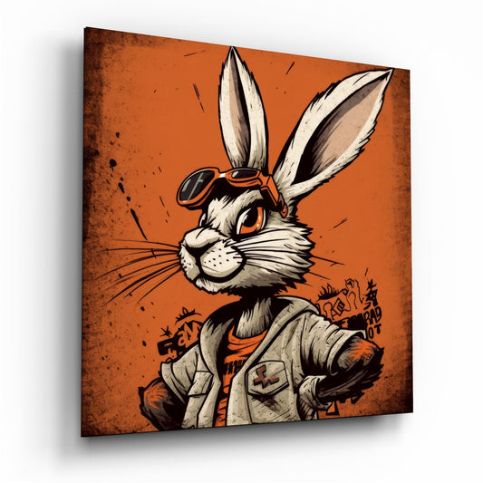 Angled front view of glass wall art featuring an illustrated white rabbit with orange eyes wearing aviator goggles and tan jacket on burnt orange background.