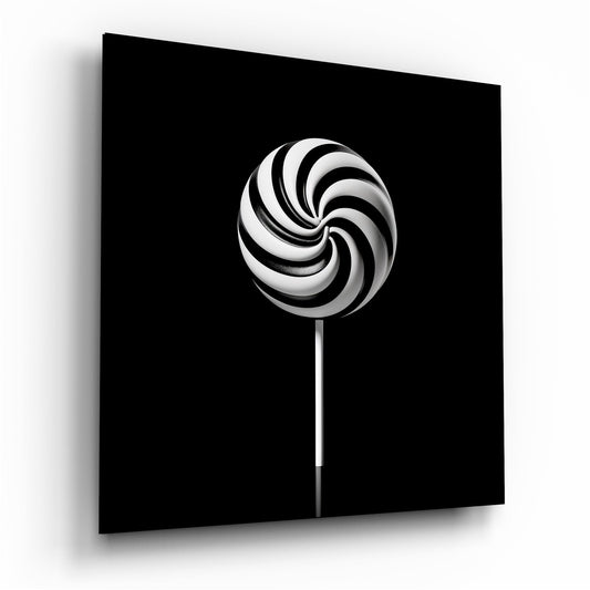 Black and white swirled lollipop with stick centered on black background, displayed as angled glass wall art panel.