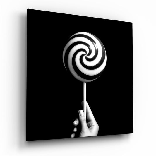 A hand holding a black and white spiral lollipop displayed against a black background on glass wall art.