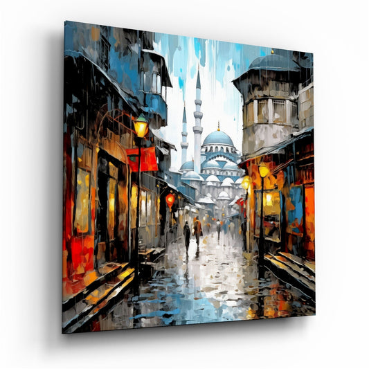 Angled perspective of a glass wall art panel displaying a wet cobblestone street lined with glowing lanterns leading to a blue-domed mosque under cloudy sky.