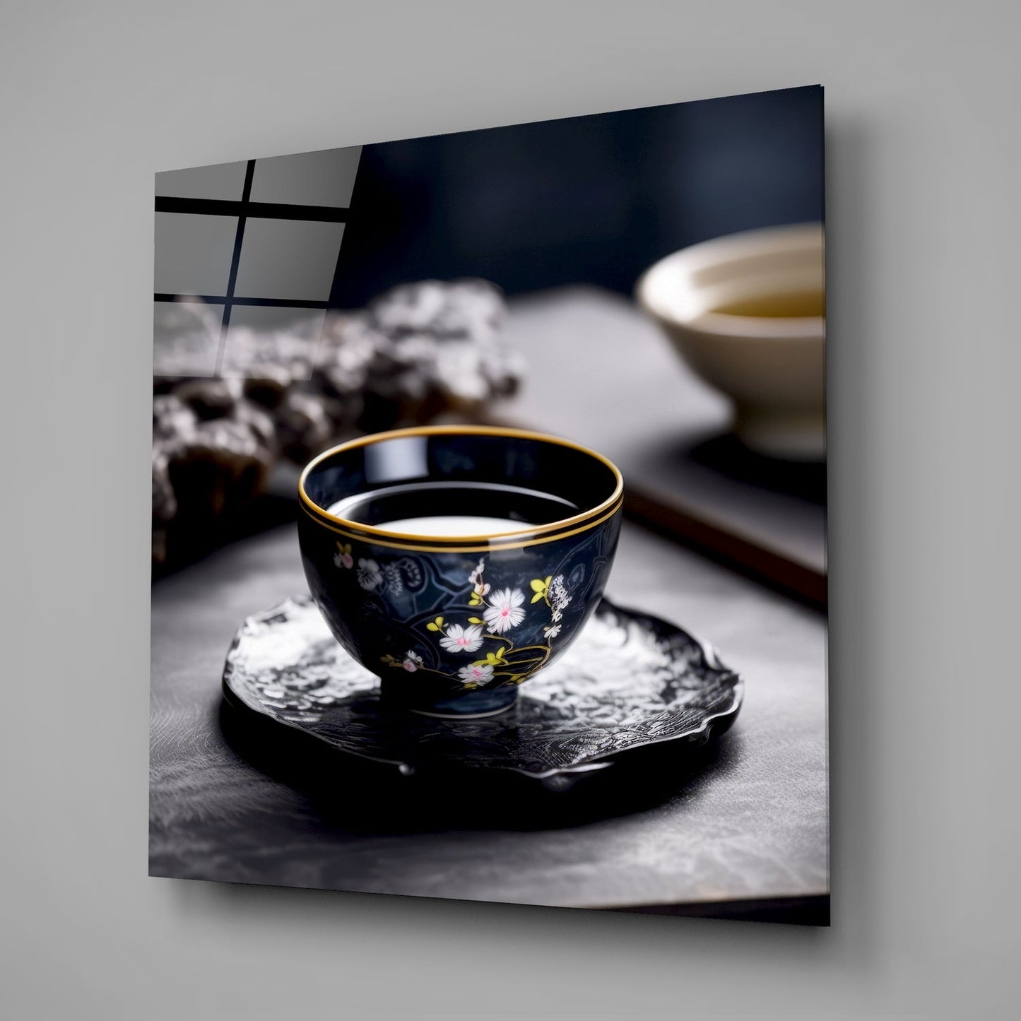 Black decorative tea bowl with gold rim and floral design sits on dark coaster, filled with light liquid, displayed on gray surface.