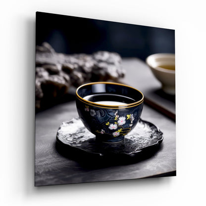 Black porcelain tea cup with gold rim and floral design sitting on dark coaster, filled with pale tea, blurred background.