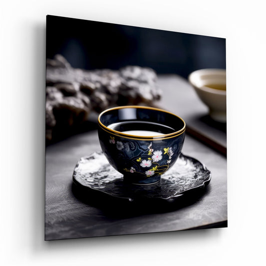 Black porcelain tea cup with gold rim and floral design sitting on dark coaster, filled with pale tea, blurred background.