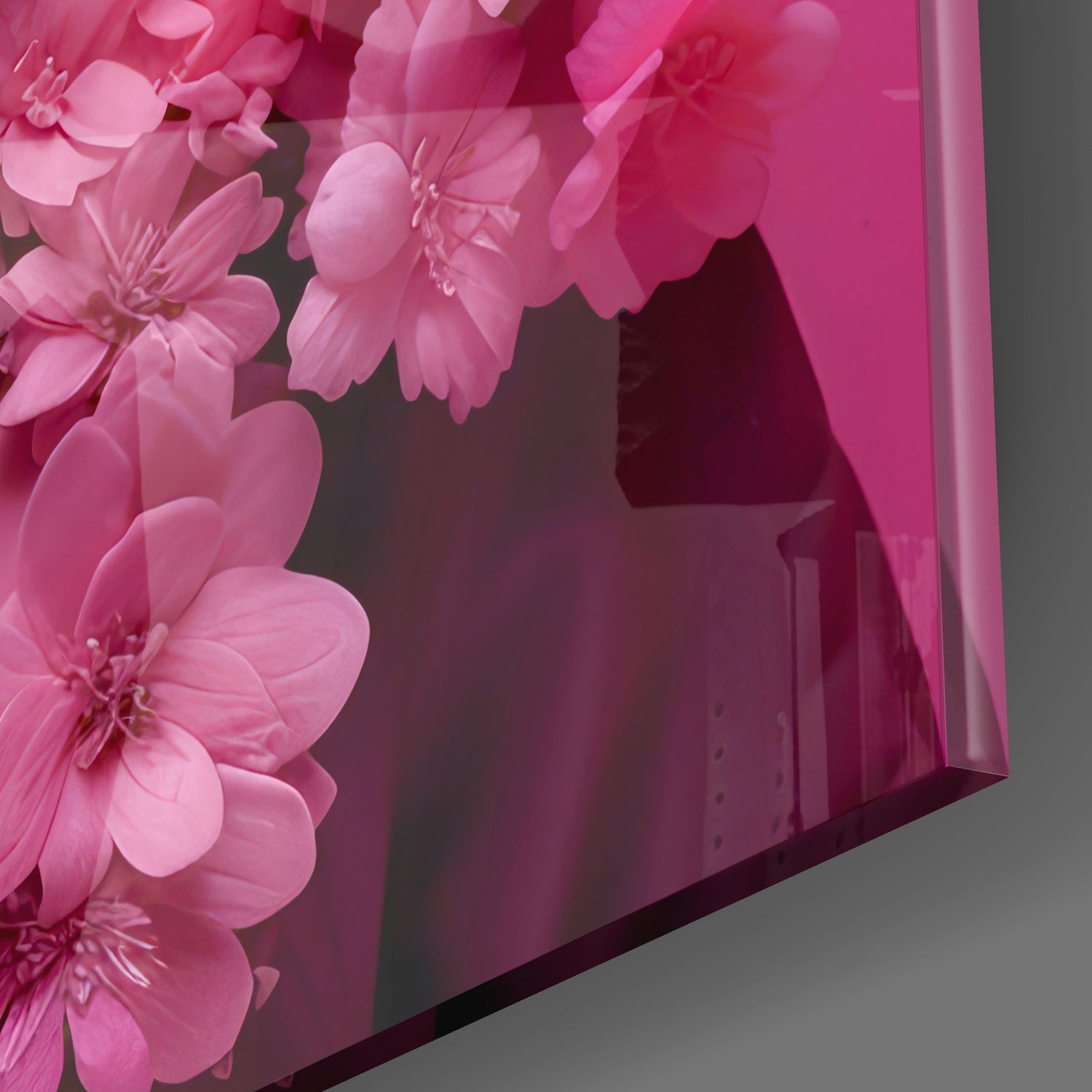 Pink flower glass wall art panel photographed at an angle, showing dimensional pink blossoms against dark background with gray surface below.