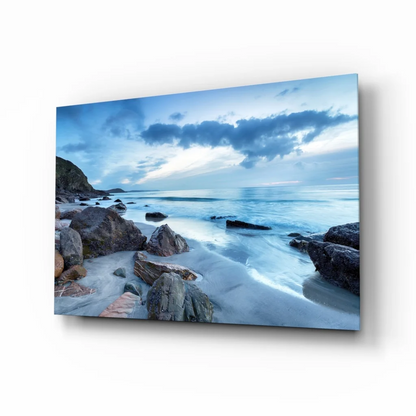 Stunning blue coastal glass wall art with smooth water, rocks, dramatic sky