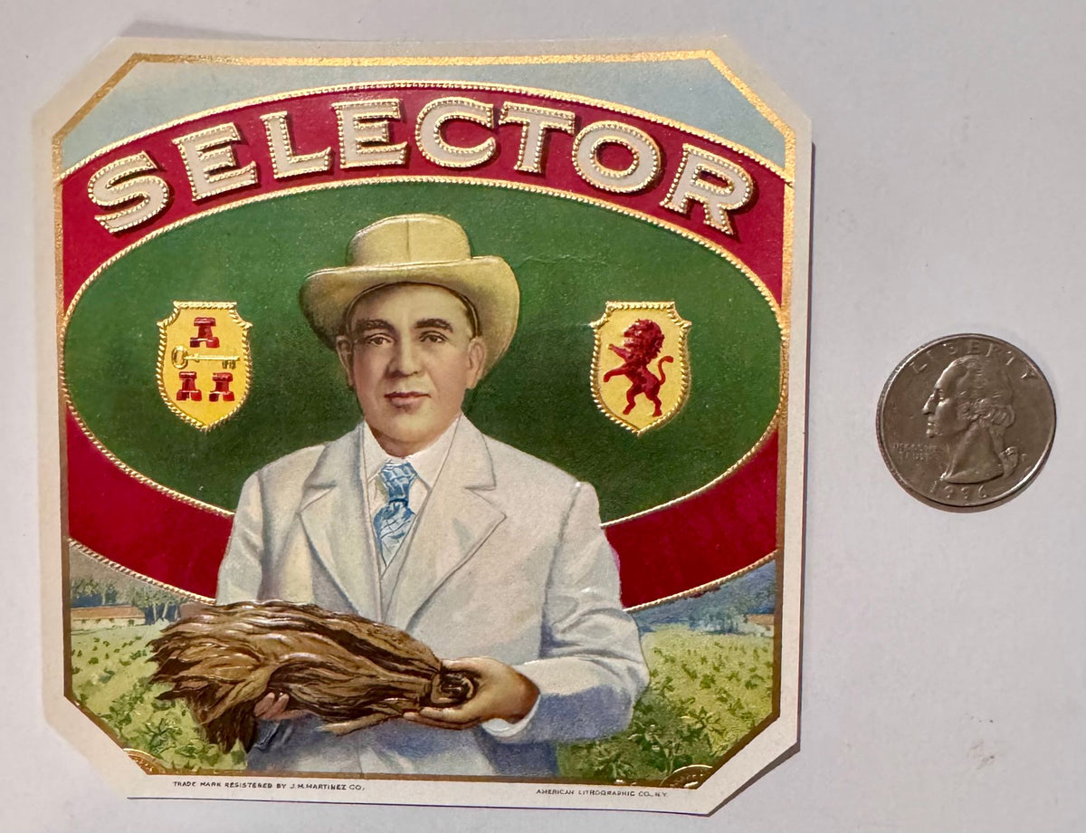 Antique Selector cigar box label beside a quarter for scale: a man in a cream suit and hat holding a hand of tobacco leaf before a tobacco field, two crest shields, SELECTOR on a red band