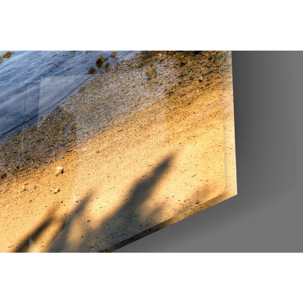 Framed glass wall art of weathered boat on sandy shore with waves and tree shadows