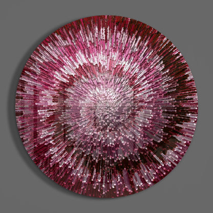 Circular glass wall art with radiating pink, red, and white glass pieces emanating from a bright center against gray background.