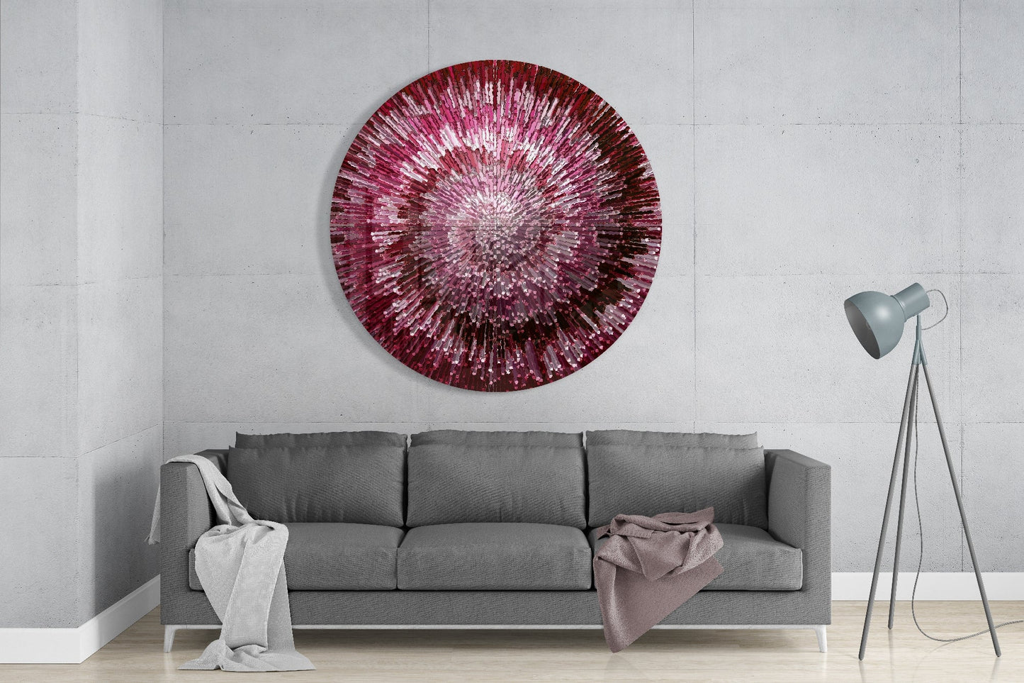 Ruby Helix glass wall art displaying radial pink and burgundy striped pattern hung above gray sofa in modern living room interior.