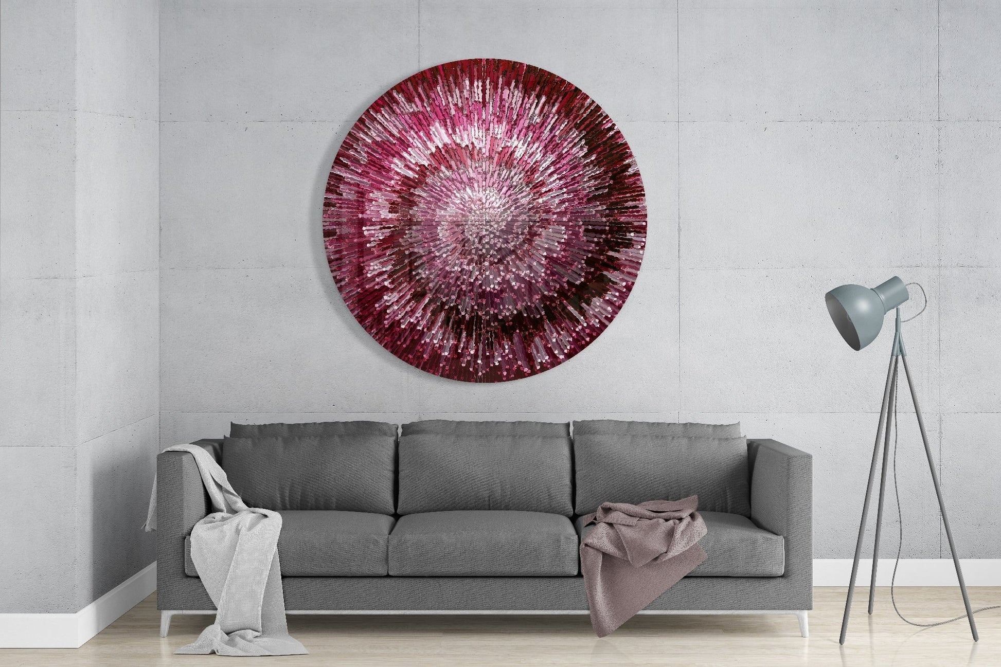 Ruby Helix glass wall art displaying radial pink and burgundy striped pattern hung above gray sofa in modern living room interior.