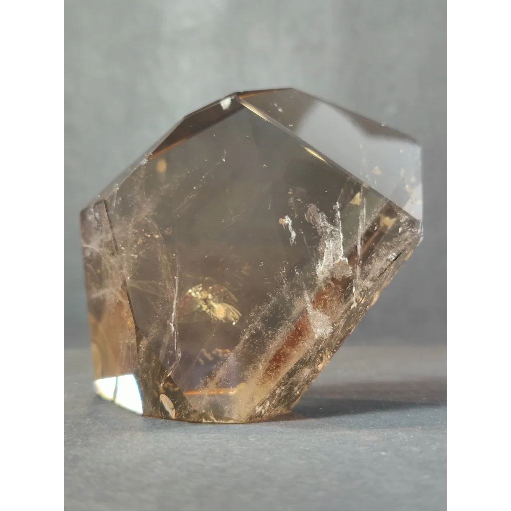 A translucent golden-brown smoky clear quartz polished free form sculpture with geometric facets and internal inclusions