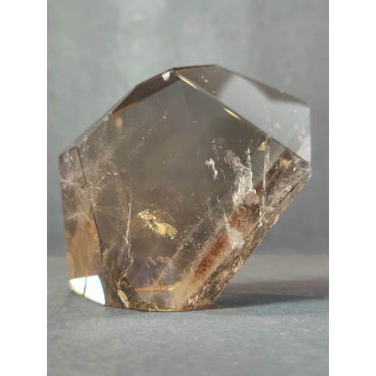 A translucent golden-brown smoky clear quartz polished free form sculpture with geometric facets and internal inclusions