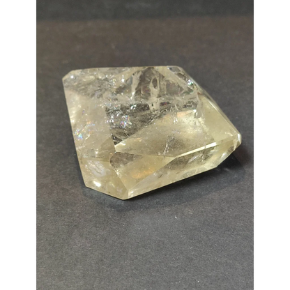 A translucent yellowish smoky clear quartz polished free form sculpture with faceted geometric shape and internal inclusions