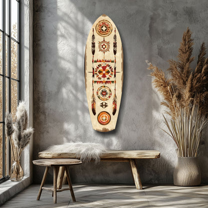 Wooden surfboard-shaped wall art with geometric Aztec patterns in red, orange, and brown hung above a wooden bench in a minimalist room with dried grasses.