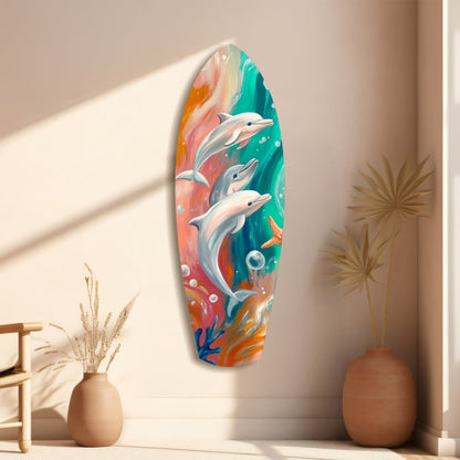 Colorful glass surfboard wall art depicting three dolphins swimming through turquoise and coral ocean waters, displayed on beige wall with decorative vases.