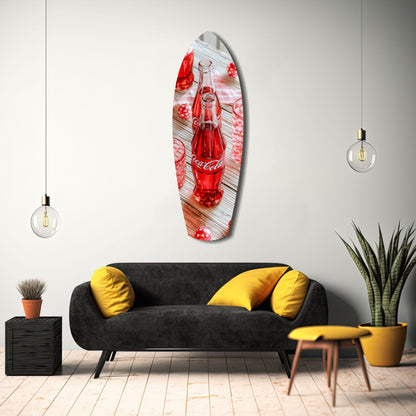 Oval glass wall art depicting a red Coca-Cola bottle on wooden background, displayed above black sofa with yellow pillows in modern interior.