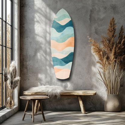 Surfboard-shaped wall art with layered wave pattern in teal, cream, and peach tones displayed above wooden bench in minimalist interior.