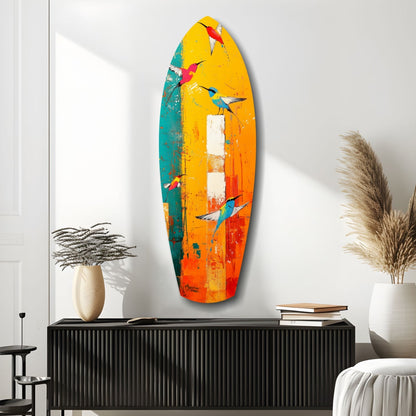 Colorful surfboard-shaped glass wall art with painted birds in yellow, orange, teal, and red tones displayed above black console table in modern room setting.