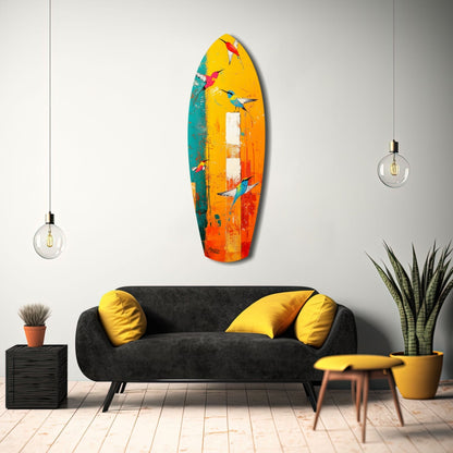 Colorful glass surfboard wall art with painted birds in yellow, orange, teal, and red tones displayed above black sofa with yellow pillows.
