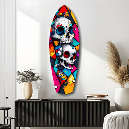Colorful glass wall art featuring two stacked skulls with vibrant geometric patterns in red, blue, yellow, and pink, displayed above a black cabinet in a minimalist interior setting.
