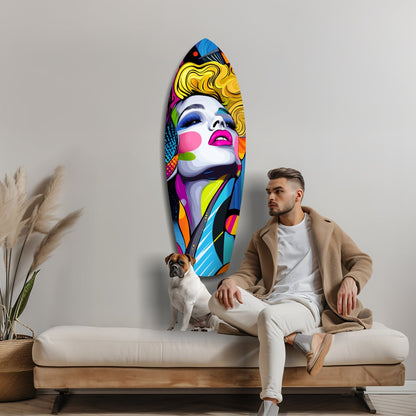 Man in beige cardigan sitting on cream sofa beside colorful pop art glass wall sculpture of blonde woman's face with vibrant geometric patterns.