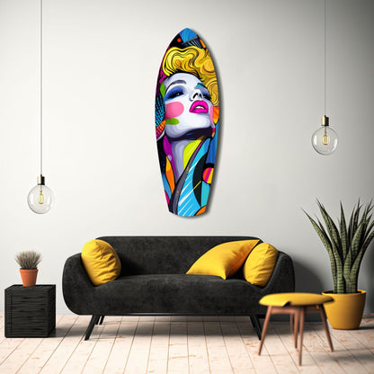 Colorful pop art glass wall panel featuring a woman's face with yellow hair and rainbow geometric patterns, displayed above a black sofa in a modern living room setting.