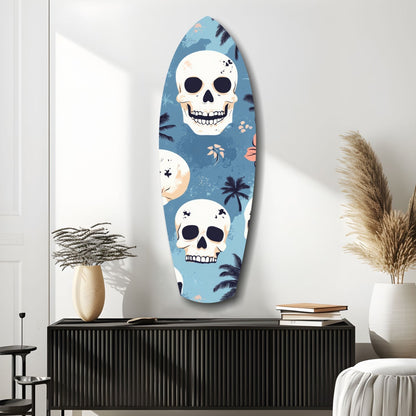 Surfboard-shaped glass wall art with blue background, white skulls, and tropical palm tree designs displayed above black cabinet in modern room setting.