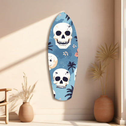 Surfboard-shaped glass wall art with blue background, white skulls, and tropical palm leaf patterns displayed on cream wall beside decorative vases.