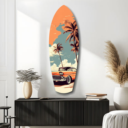 Surfboard-shaped glass wall art featuring retro illustration of orange 1950s car, palm trees, and orange sunset sky displayed above black console table.