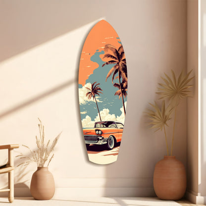 Surfboard-shaped glass wall art featuring a vintage orange car, palm trees, and sunset sky, displayed on a beige wall between two terracotta vases.