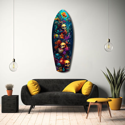 Surfboard-shaped glass wall art featuring colorful coral reef, tropical fish, and gold skulls displayed above a black sofa with yellow pillows in a modern living room.