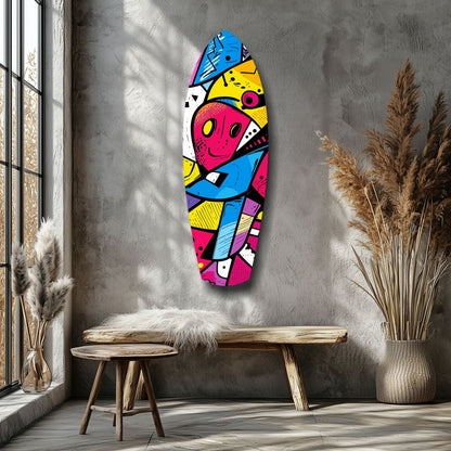 Vibrant pop-art glass wall art featuring geometric shapes and a stylized face in bright pink, blue, yellow, and black displayed above a wooden bench in a minimalist room.