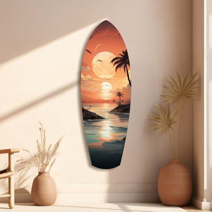 Surfboard-shaped glass wall art displaying a tropical sunset scene with palm trees, moon, and ocean, displayed on a beige wall with dried plant decor.