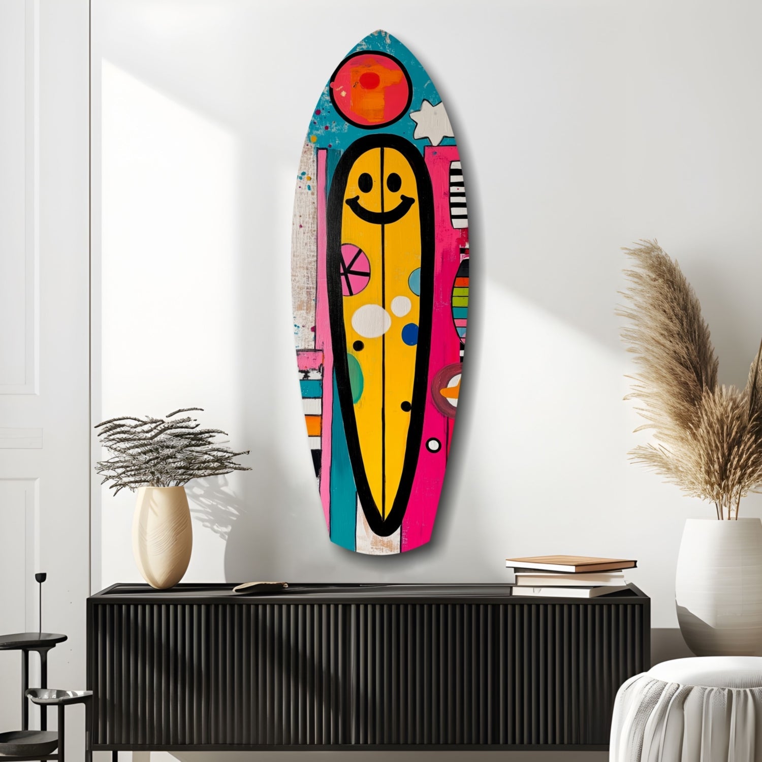 Colorful smiley surfboard wall art hanging above black cabinet between potted plants and books in minimalist interior.